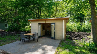 Kleine houten lodge met tuinset bij Forest Lodge in Het Amsterdamse Bos, Nederland, omringd door groen.