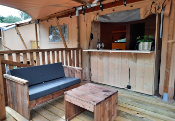 Espace salon extérieur de la Glampingtent au Het Amsterdamse Bos, Pays-Bas, avec mobilier en bois et bar.