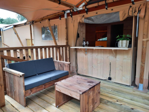 Espace salon extérieur de la Glampingtent au Het Amsterdamse Bos, Pays-Bas, avec mobilier en bois et bar.