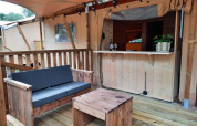 Outdoor seating area at Glampingtent in Het Amsterdamse Bos, Netherlands, with wooden furniture and bar.
