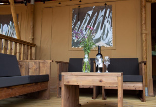 Coin salon extérieur d'une tente safari au Het Amsterdamse Bos, meubles en bois, vin et fleurs sur table.