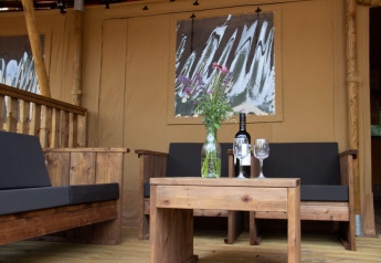 Coin salon extérieur d'une tente safari au Het Amsterdamse Bos, meubles en bois, vin et fleurs sur table.