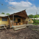 Lodge Glampingtent con grandes tiendas, terraza de madera y bancos, rodeada de árboles y luces exteriores.