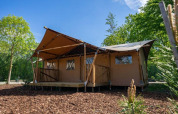 Lodge de tienda glamping en Het Amsterdamse Bos, Países Bajos, rodeada de árboles bajo un cielo soleado.