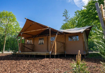 Glampingtelt-lodge i Het Amsterdamse Bos, Holland, omgivet af træer og blå himmel på en solrig dag.