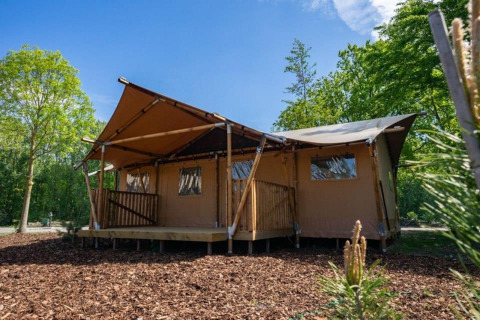 Lodge de tienda glamping en Het Amsterdamse Bos, Países Bajos, rodeada de árboles bajo un cielo soleado.