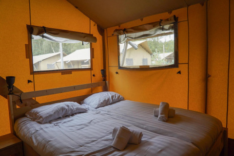Interior de una tienda glamping en Het Amsterdamse Bos, Países Bajos, con cama doble y ventanas grandes.