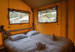 Interior de una tienda glamping en Het Amsterdamse Bos, Países Bajos, con cama doble y ventanas grandes.