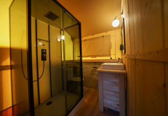Badezimmer in einem Glampingtent im Het Amsterdamse Bos, Niederlande, mit moderner Dusche und Holzwänden.