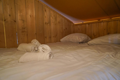 Gemütliches Bett mit weißen Handtüchern und Kissen in einem Glampingtent im Het Amsterdamse Bos, Niederlande.