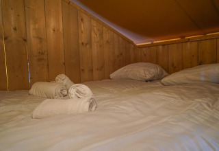Gemütliches Bett mit weißen Handtüchern und Kissen in einem Glampingtent im Het Amsterdamse Bos, Niederlande.