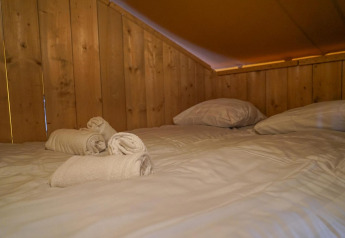 Hyggelig seng med hvide håndklæder og puder i Glampingtent på Het Amsterdamse Bos i Holland.