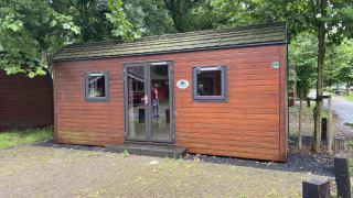Photo d’une petite maison en bois nommée Pod, entourée d’arbres, située dans un camping paisible.