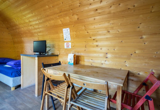 Interior de una pequeña casa de madera con mesa de comedor, sillas, cama y TV, Pod en Het Amsterdamse Bos.
