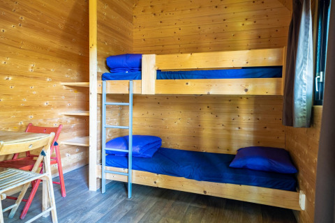 Interior de madera de una pequeña casa Pod en Het Amsterdamse Bos con literas, ropa azul y mesa.