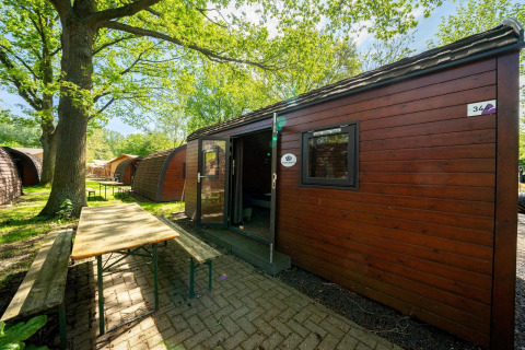Vista exterior de una casa diminuta Pod en Het Amsterdamse Bos, Países Bajos, con bancos y mesa frente.