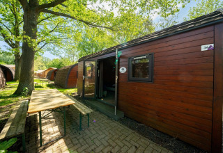 Vista exterior de una casa diminuta Pod en Het Amsterdamse Bos, Países Bajos, con bancos y mesa frente.