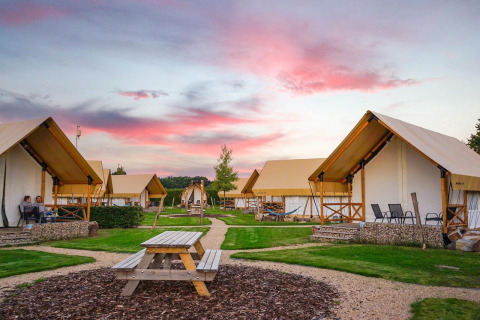 Site de glamping avec tentes confortables et bancs de pique-nique sous un ciel de coucher de soleil.