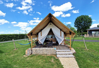A photo of a stylish glamping tent cabin featuring a porch, outdoor seating, and green lawn under blue sky.
