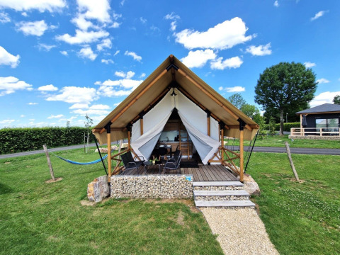 Photo d’un hébergement glamping élégant avec tente, terrasse aménagée et pelouse verdoyante sous ciel bleu.