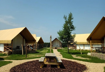 Glampingverblijf met canvas tenten, picknicktafel en grindpaadjes onder een stralend blauwe lucht.