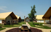 Site de glamping avec tentes modernes, table de pique-nique et allées gravillonnées sous ciel bleu.