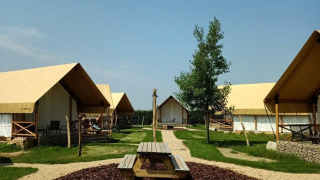 Site de glamping avec tentes modernes, table de pique-nique et allées gravillonnées sous ciel bleu.