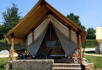 Glamping accommodation with canvas tent, raised wooden deck and chairs in a peaceful outdoor setting.