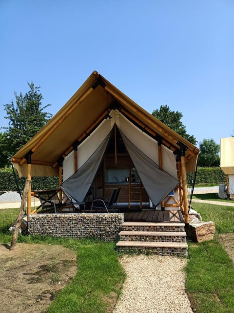 Hébergement glamping avec tente en toile, terrasse surélevée en bois et chaises dans un cadre verdoyant.