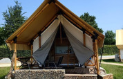 Hébergement glamping avec tente en toile, terrasse surélevée en bois et chaises dans un cadre verdoyant.