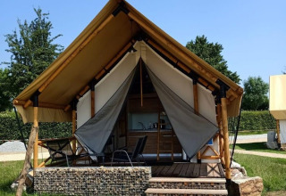 Hébergement glamping avec tente en toile, terrasse surélevée en bois et chaises dans un cadre verdoyant.