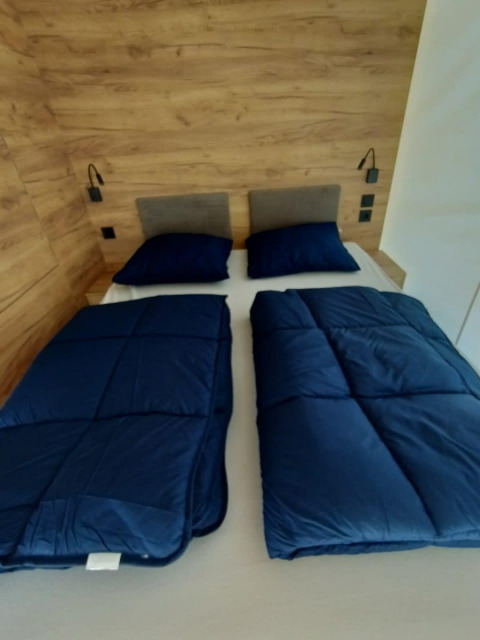 Habitación de glamping con cama doble, dos almohadas y edredones separados azul marino junto a pared de madera.