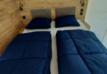 Hébergement glamping avec lit double, deux oreillers et couettes séparées bleu marine contre un mur en bois.