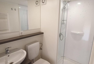 Salle de bain moderne dans un glamping avec douche, toilettes, lavabo et sol en bois clair.