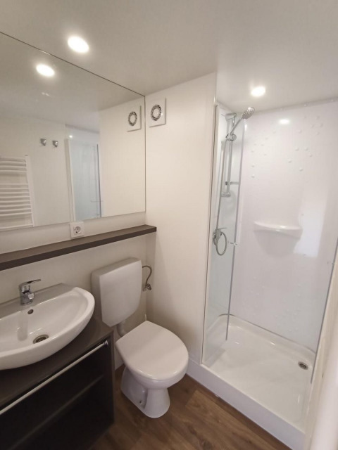 Salle de bain moderne dans un glamping avec douche, toilettes, lavabo et sol en bois clair.