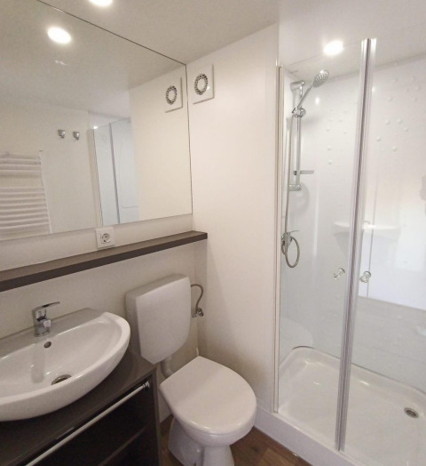 Salle de bain moderne en glamping avec lavabo, toilettes, grande douche vitrée et ambiance lumineuse.