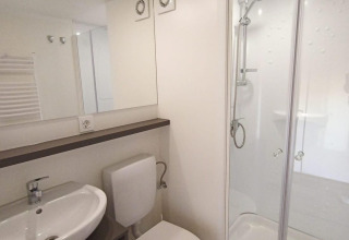 Baño moderno de glamping con lavabo, inodoro, amplio espejo, ducha y una decoración minimalista.