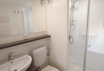 Salle de bain moderne en glamping avec lavabo, toilettes, grande douche vitrée et ambiance lumineuse.