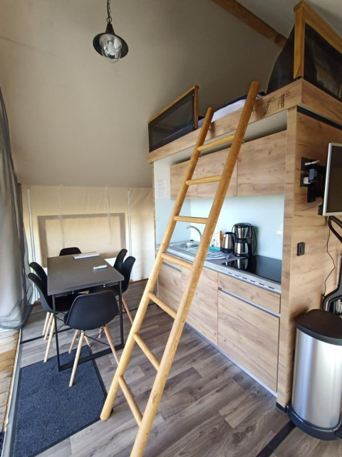 Intérieur d'un hébergement glamping avec coin cuisine, table à manger, échelle vers mezzanine et équipements modernes.