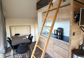 Intérieur d'un hébergement glamping avec coin cuisine, table à manger, échelle vers mezzanine et équipements modernes.
