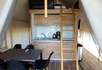 Glamping tent interieur met keukentje, zwarte stoelen, eettafel, houten vloer en bed op de mezzanine.