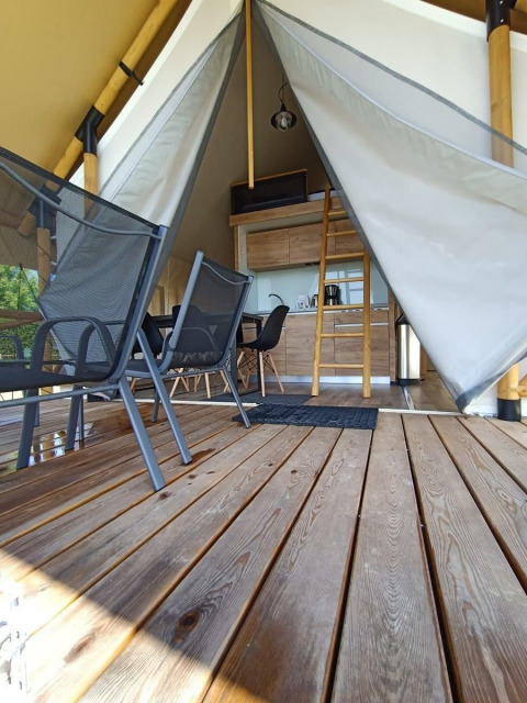 Vista interior de una tienda de glamping con terraza de madera, mesa, sillas y altillo accesible por escalera.