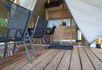 Vista interior de una tienda de glamping con terraza de madera, mesa, sillas y altillo accesible por escalera.