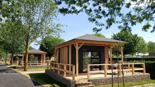 Casa pequeña moderna con porche de madera en entorno verde y soleado, perfecta para descansar.