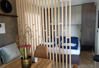 Innenaufnahme eines Tiny House bei Poort van Maastricht mit Holztrennwand, Esstisch und Bettbereich.