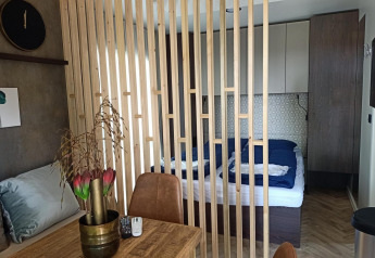 Interiør af Tiny House ved Poort van Maastricht, med træskillevæg, spisebord og udsigt til soveplads.