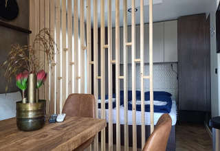 Interior de una tiny house en Poort van Maastricht, Países Bajos, con dormitorio separado por listones de madera.