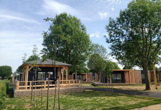 Tiny House bij Poort van Maastricht in Nederland, omgeven door bomen en groen onder een blauwe hemel.