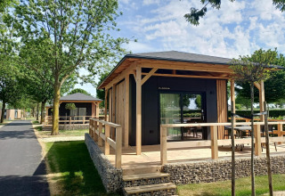 Tiny house bij Poort van Maastricht, Nederland, met houten terras en omgeven door bomen en groen.