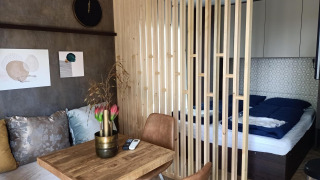Interno moderno di Tiny House con separatore in legno, zona letto, tavolo da pranzo e divano accogliente.